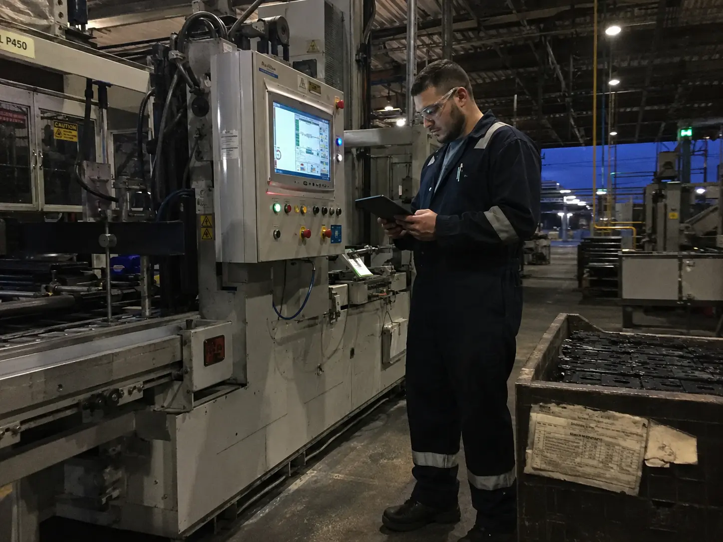 Tecnico controlla da tablet un pannello di controllo collegato a un macchinario industriale in fabbrica
